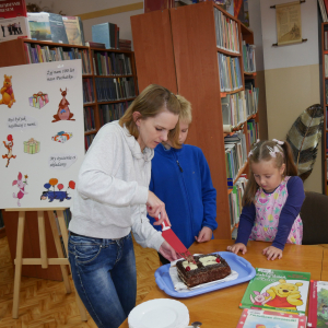 Uczestniczka zajęć kroi tort, dziewczynka i chłopiec przygląda się tej czynności