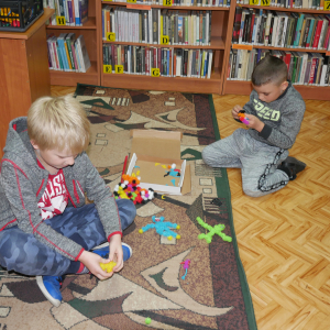 Dwóch chłopców siedzi na dywanie  bawią się kolorowymi rzepami Clingabeez