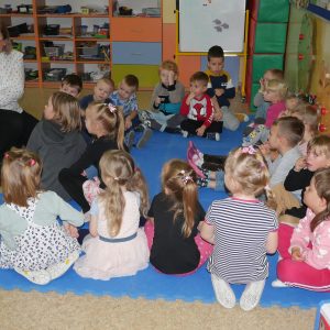 Przedszkolaki siedzą na dywanie Pani bibliotekarka pokazuje książeczkę