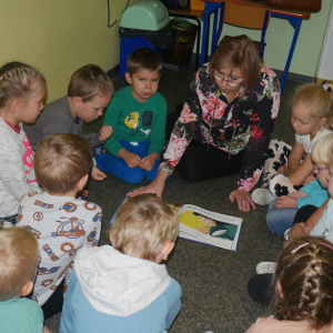 Dzieci siedzą na dywanie Pani bibliotekarka czyta książeczkę dzieciom