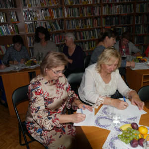 Uczestnicy spotkania  siedzą przy stolikach piszą