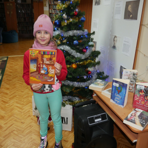 Dziewczynka stoi przy choince z książką w dłoniach
