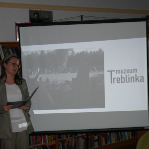 Kobieta przemawia do uczestników spotkania, w tle prezentacja Muzeum Treblinka