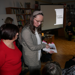Kobieta prezentuje uczestnikom spotkania tomik poezji