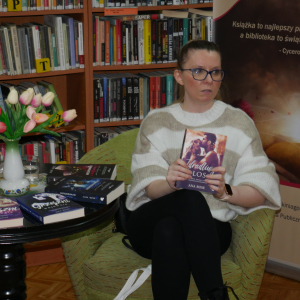 Pisarka Ana Rose siedzi w fotelu, trzyma w dłoniach książkę