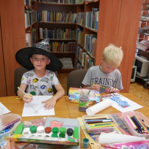 Dwóch chłopców koloruje kolorowanki.W tle regały z książkami.