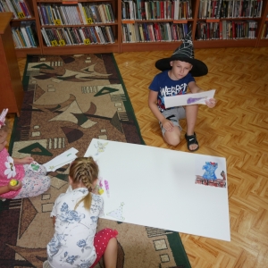 Dwie dziewczynki i jeden chłopiec naklejają swoje kolorowanki na tablice.