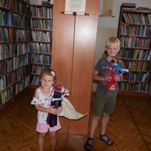 Dziewczynka i chłopiec prezentują swoje Potworki.W tle regały z książkami.
