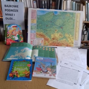 Na stoliku rozłożone podróżnicze książki i mapa Polski. W tle regały z książkami.
