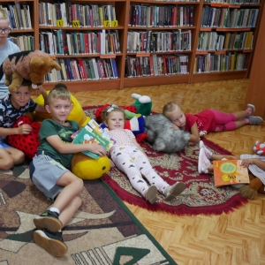 Dzieci pozują do zdjęcia-leżą na dywanie  trzymając książki i maskotki.