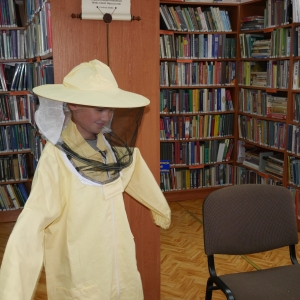 Chłopiec w stroju pszczelarza, w tle regały z książkami.