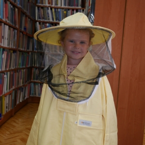 Dziewczynka w stroju pszczelarza, w tle regały z książkami.
