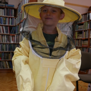 Chłopiec w stroju pszczelarza, w tle regały z książkami.