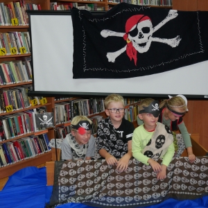Dzieci w strojach pirackich pozują  do zdjęcia, nad nimi bandera piratów.