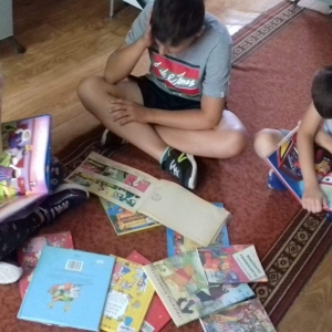 Dzieci siedzą na dywanie i czytają książeczki.
