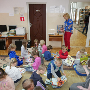 Przedszkolaki siedzą na dywanie i oglądają książeczki