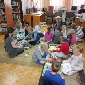 Przedszkolaki siedzą na dywanie i oglądają książeczki